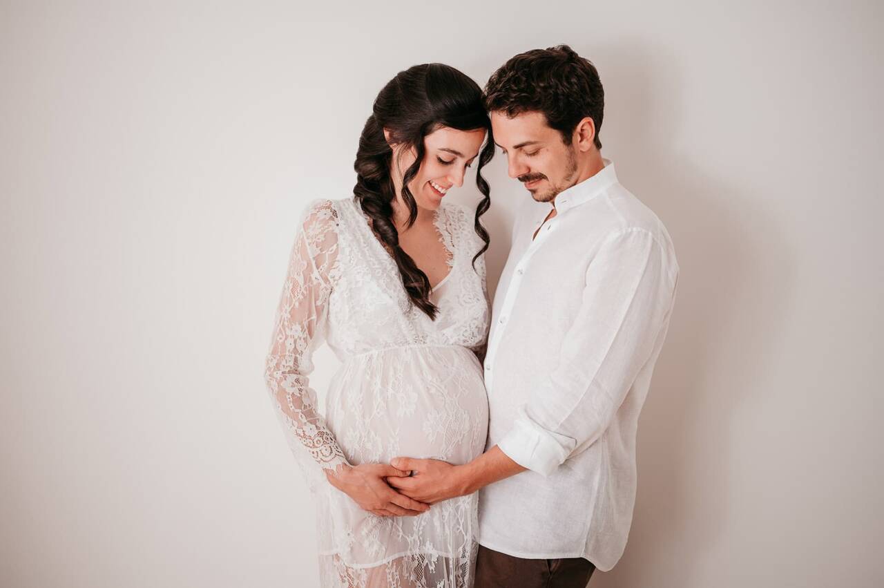 Futura mamma e futuro papà fotografati in stile minimal con abiti bianchi che hanno fatto la sessione fotografica di gravidanza al momento giusto